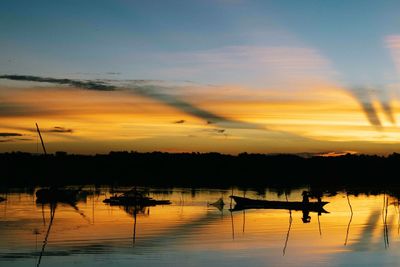 Silhouette boats in calm lake at sunset