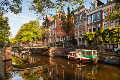 Boats moored in canal by city against trees