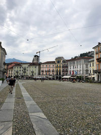 People walking on footpath by buildings in city against sky