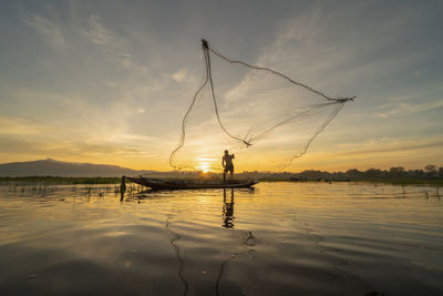 Man fishing in lake against sky during sunset