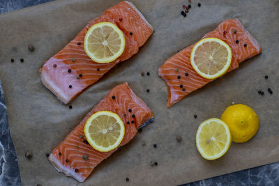 Three row salmon fish fillet uncooked with  spices and lemon slice on it on a backing paper.