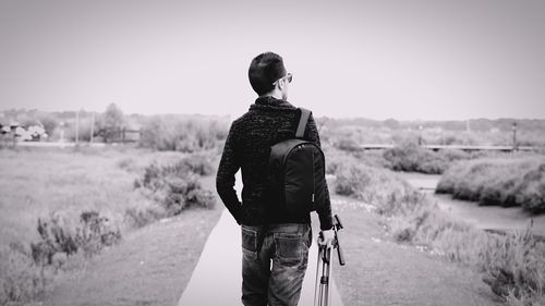 Rear view of backpack man with tripod walking on footpath