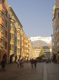 People on street amidst buildings in city against clear sky