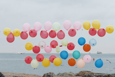 Colorful balloons by sea against sky