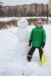 Happy satisfied boy standing nearby huge snowman. winter fun in the snow park.