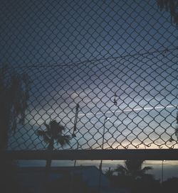 Man standing by chainlink fence against sky