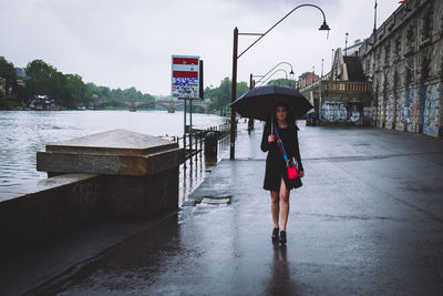Full length of woman standing on wet road during rainy season