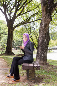 Portrait of young woman wearing hijab using mobile phone while sitting in park