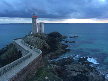 Lighthouse by calm blue sea against sky