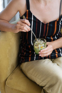 From above crop woman enjoying dessert and eating jelly with spoon from glass in cafe