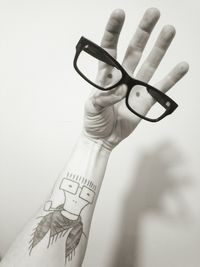 Close-up of human hand with tattoo holding eyeglasses against wall