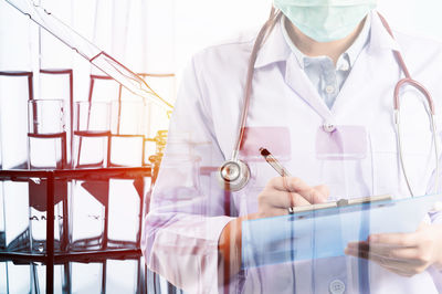 Double exposure of female doctor writing on clipboard with chemicals in laboratory