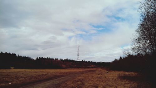 Electricity pylon on field against cloudy sky