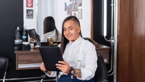 Smiling young woman looking at mirror while sitting at salon