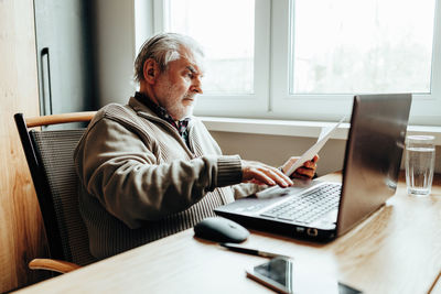 An elderly man works at a laptop, learning from home, home bookkeeping