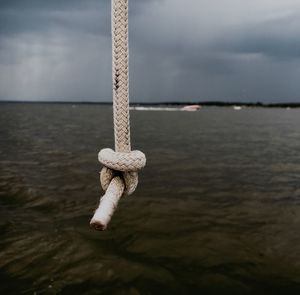 Close-up of rope hanging on sea against sky