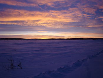 Scenic view of snow covered land against sky during sunset