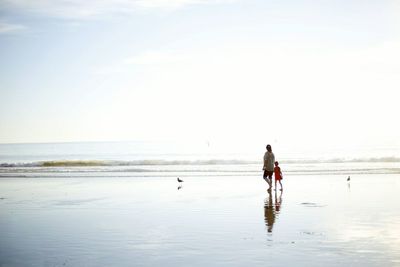 Mother and daughter walking along wet sandy beach