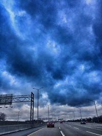 Cars on road against cloudy sky