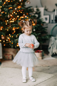 A beautiful little girl in a festive dress is standing at the christmas tree. 