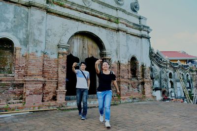 Happy friends taking selfie through smart phone while walking against historic building
