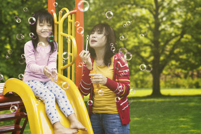 Happy mother and daughter enjoying bubbles in park