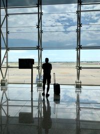 Rear view of man looking through window while standing at airport