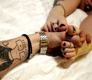 Cropped tattooed hand holding woman legs on bed at home