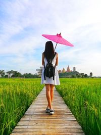 Rear view of woman walking on field against sky