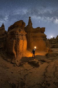 Silhouette of unrecognizable explorer standing with flashlight on scenery of rocky formations in highlands under milky way starry sky in goblin valley state park, utah, usa.