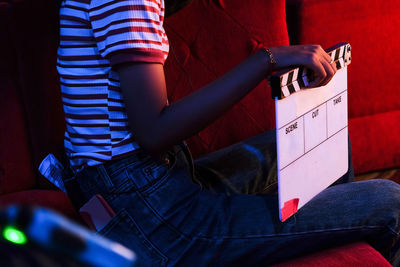 Midsection of woman holding film slate while sitting on chair