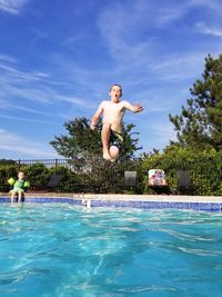 Boy jumping in swimming pool against blue sky
