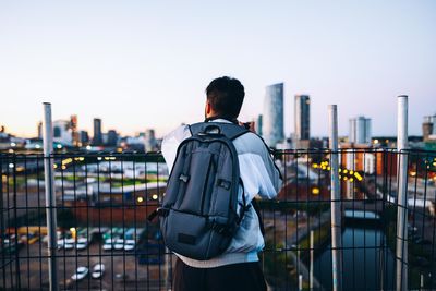 Rear view of man standing by railing against buildings