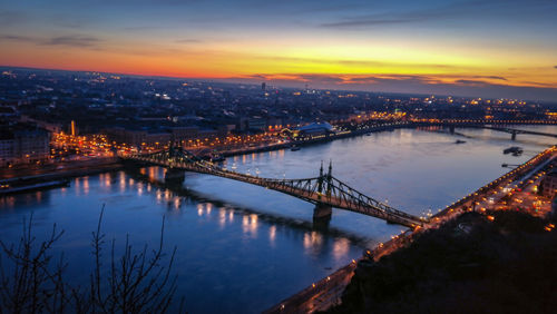 Illuminated bridge over river in city against sky at sunset