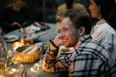 Side view of smiling young man leaning on elbow at dining table during sinner party