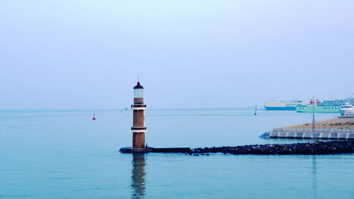 Lighthouse by sea against clear sky