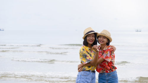 Cheerful kids standing at beach against sky