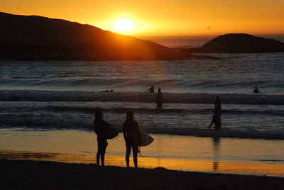 Silhouette women standing at beach against sky during sunset