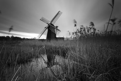 Traditional windmill on grassy field against cloudy sky