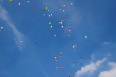 Low angle view of helium balloons flying against sky