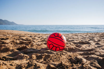 Red football ball laying on the beach with sea at the background