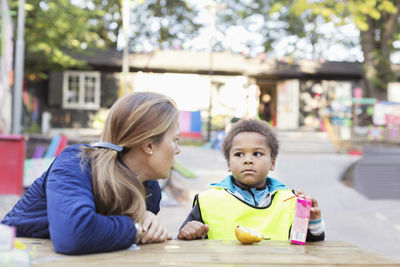 Angry teacher looking at student holding juice box outside kindergarten