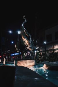 Statue by illuminated city against sky at night