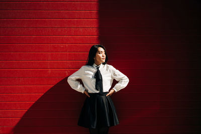 Portrait of young woman standing against red wall