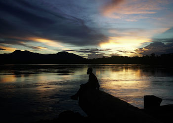 Silhouette man by lake against sky during sunset