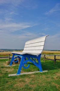 Empty bench on field against sky