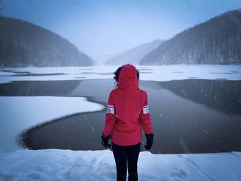 Rear view of woman with red coat standing in front of a frozen lake during winter