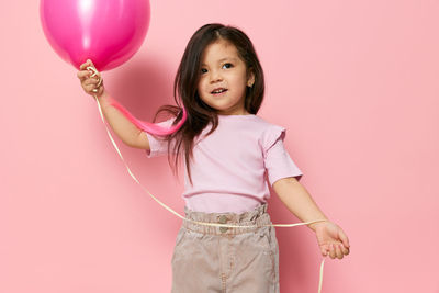 Portrait of young woman with balloons against pink background