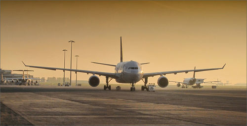 Airplane on airport runway against clear sky during sunset