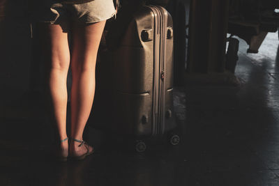 Low section of young woman with luggage standing on tiled floor at railroad station platform